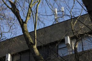 Image depicts cellular antennas installed on top of a building. Image partially obscured by a tree.