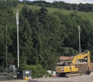 Three masts in a construction area with a hill behind
