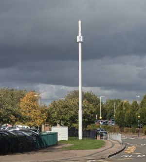 Shows a monopole with various antennas for Three, you can see it being placed close to a car park on both sides.